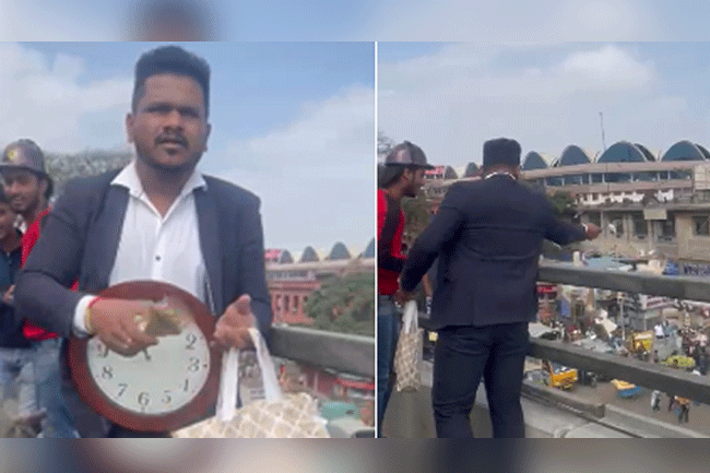 Man wearing suit, with wall clock hanging from neck throws currency notes from flyover in B'luru